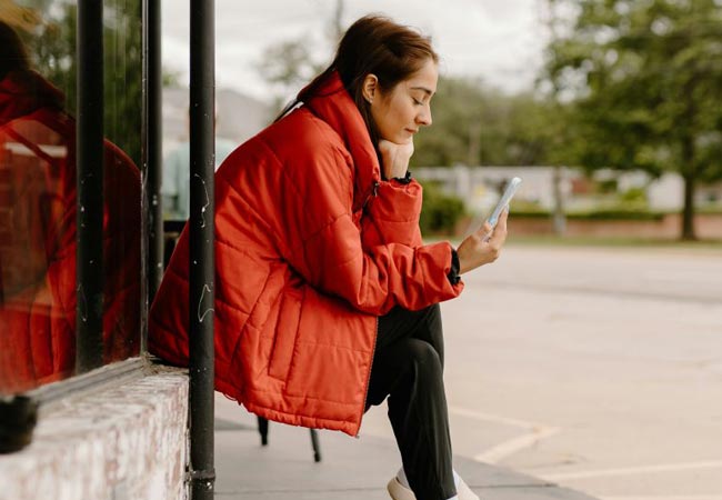 A person in a red coat sat outside looking at her phone