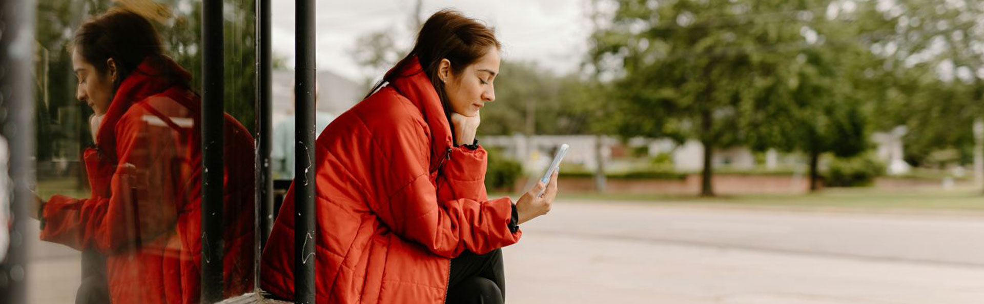Young person in a red coat sat outside looking at her phone